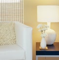 Modern home interior decor. Living room with chair, pillow, table, lamp, painted wall, window blinds and flowers in vase.