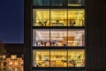 A contemporary office with a broad modern, glazed facade featured by square pattern of wide glazed windows illuminated at night