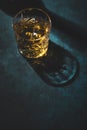 Contemporary still life with whiskey, scotch or bourbon glass with ice on textured blue background with hard lights and shadows,