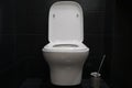 Contemporary white wall hung toilet. Black shiny tiles. Modern bathroom design. Cleanliness and hygiene