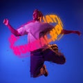 Contemporay artwork. Young man with neon lettering around body dancing isolated over blue background in neon light