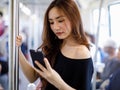 Content Asian female riding train and chatting on social media via smartphone and looking at phone screen. Communication and