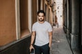 Content attractive hispanic man in white tshirt walking old town streets holding mobile phone hand.Bearded hipster male Royalty Free Stock Photo