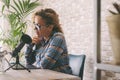 Content creator adult woman recording a podcast interview using microphone and laptop sitting at the desk. Home office workstation