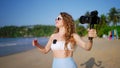 Female influencer records beach lifestyle with pro camera and wireless lav mic. Content creator films tropical travel