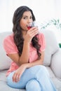 Content cute brunette sitting on couch drinking glass of juice Royalty Free Stock Photo