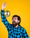 Content man in checkered shirt with happy face holding shining disco ball posing on yellow, party fun