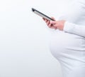 Content pregnant woman holding her tablet sitting on a couch in the living room at home