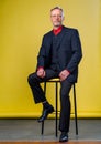 Content senior business man smiling in a dark suit. Handson legs . Red shirt. Confident. Business style concept