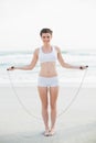 Content slim brown haired model in white sportswear playing with a skipping rope