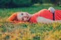 Content young model with red head long hair lying on grass in summer park smiling Royalty Free Stock Photo