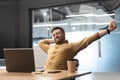 Contented Businessman Near Laptop Stretching Arms Relaxing Sitting In Office