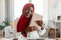 Contented buyer, shopaholism and commerce concept. Happy african american lady in hijab hugging cardboard box