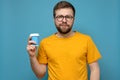 Contented, calm man with round glasses and a yellow tee-shirt is holding a disposable paper cup in hand, on a blue