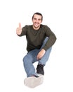 Contented casual young man sitting on the floor smiles to camera, showing thumb up approval gesture. Lifestyle full length Royalty Free Stock Photo