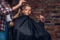 Contented cute preschooler boy shows thumbs up while getting a haircut. Children hairdresser with scissors and comb is