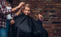 Contented cute preschooler boy shows thumbs up while getting a haircut. Children hairdresser with scissors and comb is