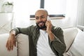 Contented latin man talking on cellphone and smiling while sitting on sofa at home, having pleasant conversation Royalty Free Stock Photo