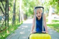 A contented little girl in a blue dress is standing alone in the street with a yellow suitcase and waiting for her