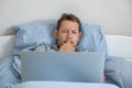 Contented young businessman freelancer work on laptop laying in bed at home. Male professional trader investor working Royalty Free Stock Photo