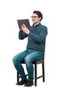 Contented young male student, seated on a chair, using a PC tablet for entertaining. Modern education concept, working and Royalty Free Stock Photo