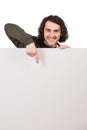 Contented young man standing behind a blank banner for advertising and messages, pointing index finger to the empty sheet, copy Royalty Free Stock Photo