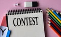 CONTEST - a word written in a notebook on a pink background and colored pencils Royalty Free Stock Photo