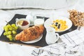 Continental breakfast in bed. Croissant, cornflakes, tea, milk and fruit on black tray Royalty Free Stock Photo