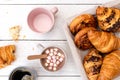 Continental breakfast with hot chocolate with marshmallows, black coffee and basket of pastries. Half eaten on white wood from Royalty Free Stock Photo