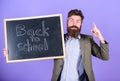 Continue your education with us. Teacher bearded man stands and holds blackboard with inscription back to school violet