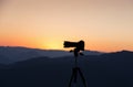 A contour of a camera on a tripod against the background of a mountain landscape.
