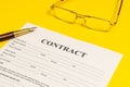 Contract formation elements on yellow office desk with glasses and pen