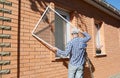 Contractor installing mosquito wire screen on house window to protect from insects. Royalty Free Stock Photo