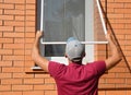 Contractor installing mosquito wire screen on house window to protect from insects. Mosquito wire screen installation