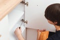 Man assembling white wooden furniture with a screwdriver. Housing furniture theme