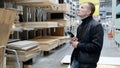 Contractor using his smartphone to plan a renovation project and select materials in a bustling lumber yard, while Royalty Free Stock Photo
