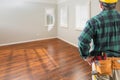 Contractor Wearing Toolbelt and Hard Hat Facing Empty Room with Hard Wood Floors