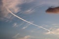 Contrail in blue sky, wispy white clouds behind