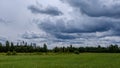 Contrast rain storm clouds over green meadow and some trees in summer. blue sky before the rain Royalty Free Stock Photo