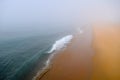 Vibrant Turquoise Ocean Wave Disappears into the Fog Along a High Contrast Orange Sandy Beach Royalty Free Stock Photo