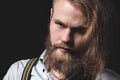 Contrasting low key portrait of a bearded long-haired stylish brutal man in a gray shirt with suspenders sternly looks