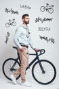 Convenient way to travel. Full length of a modern looking man with beard pulling his bicycle while standing against grey Royalty Free Stock Photo