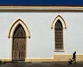 Old white colonial church facade with carved wooden door and window with a man walking