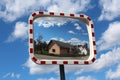 Convex rectangular traffic mirror mounted on metal pole with neighborhood and road in reflection on cloudy blue sky background