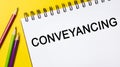 Conveyancing on a white notepad with pencils on a yellow background. Business concept