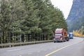 Convoy of the big rig semi trucks with loaded semi trailers led by burgundy semi truck with flat bed semi trailer driving on the Royalty Free Stock Photo
