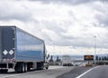 Convoy of big rigs semi trucks with different semi trailers running on the interstate highway with bridge and road sign electronic Royalty Free Stock Photo