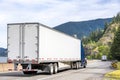 Convoy of the big rigs semi trucks with dry van semi trailers transporting cargo driving on the winding road with river and Royalty Free Stock Photo