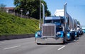 Convoy of big rigs semi trucks on the road with blue classic American bonnet semi tractor with bulk trailer