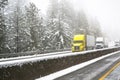 Convoy of big rigs semi trucks with semi trailers moving cautiously on a highway during a winter blizzard near Shasta Lake in